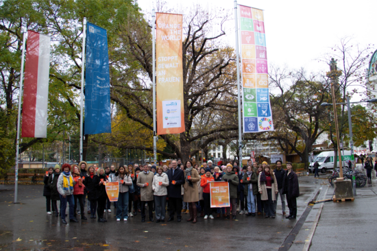 Gruppenfoto mit etwa 45 Personen im Resselpark vor einer Reihe von Flaggen. Eine davon Orange-the-World. Der Boden ist regennass.