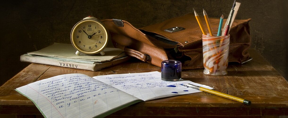Wooden table with an open notebook, pens and a clock