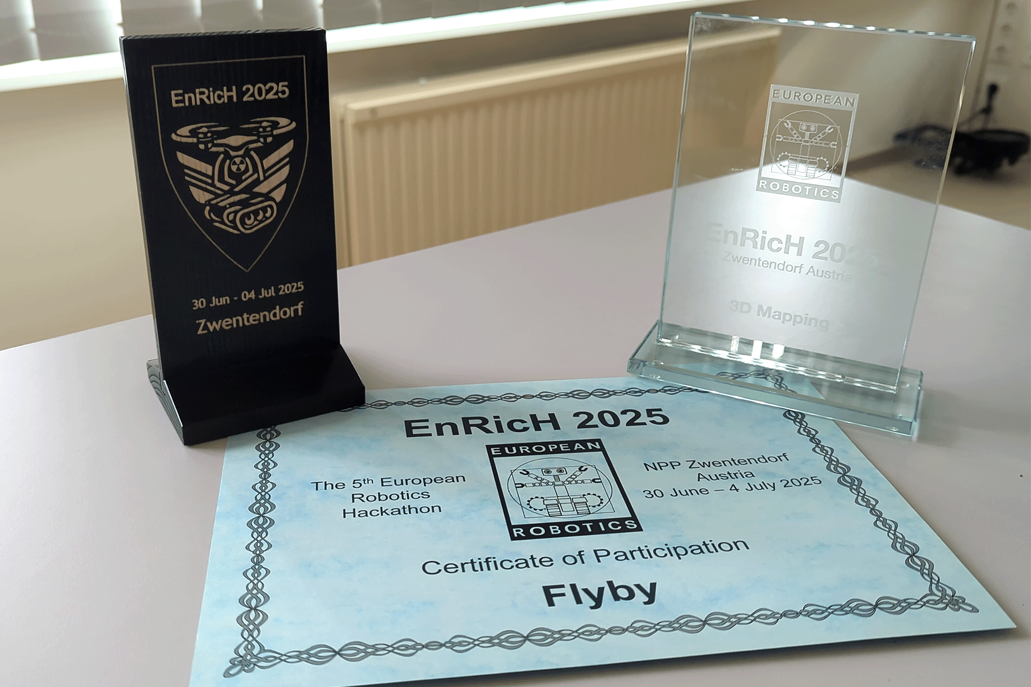 Urkunde des EnRicH Wettbewerbs und zwei gewonnene Pokale, darunter ein gläserner als Preis