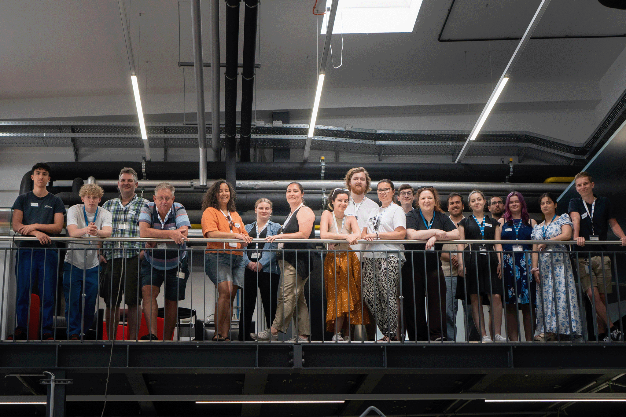 Gruppenfoto in einem Innenraum. Die Personen stehen an einem Geländer, Rohre im Hintergrund sichtbar