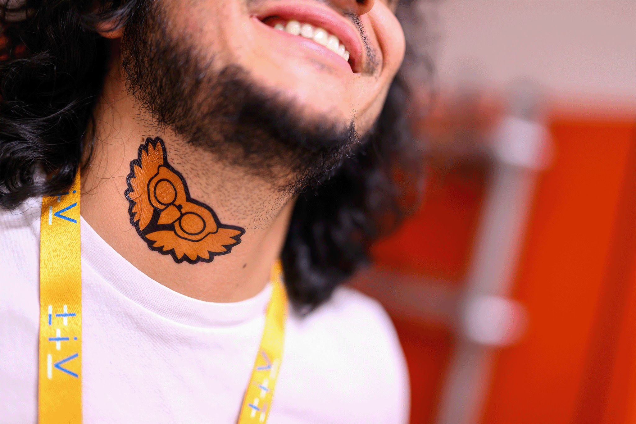 Adhesive tattoo on the neck of a person smiling. A mixture of eagle and owl in orange.