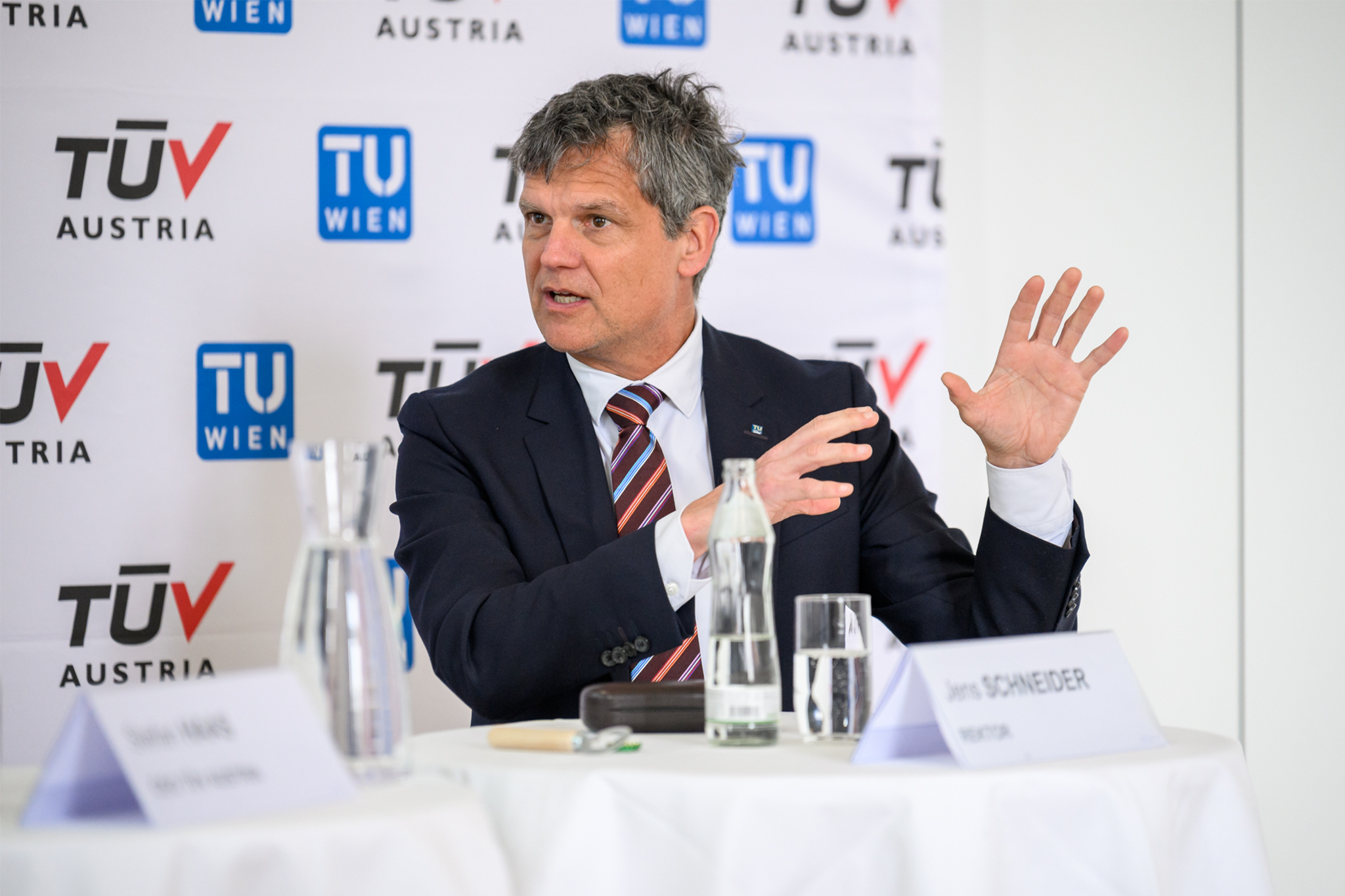 Rektor Jens Schneider im Jackett vor einer TUW und TÜV-Logos beim Sprechen