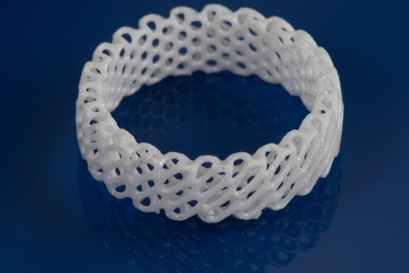 Ein 3D-gedruckter, weißer Keramikring mit komplexer Struktur auf einer blauen Fläche.