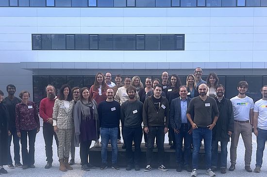Gruppenfoto mit 27 Personen, im Hintergrund ist ein modernes Gebäude zu sehen.