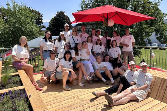Team: menschen in weißen T-Shirts stehend und sitzend, rechts hinten großer roter Sonnenschirm