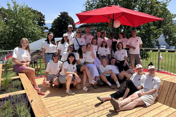 Team: menschen in weißen T-Shirts stehend und sitzend, rechts hinten großer roter Sonnenschirm