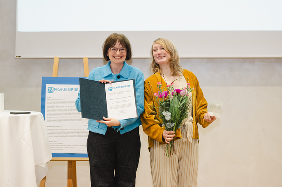 Vizerektorin Koch und Frauenpreisträgerin Wieser halten Urkunde und Blumenstrauß mit fröhlichem Gesichtsausdruck
