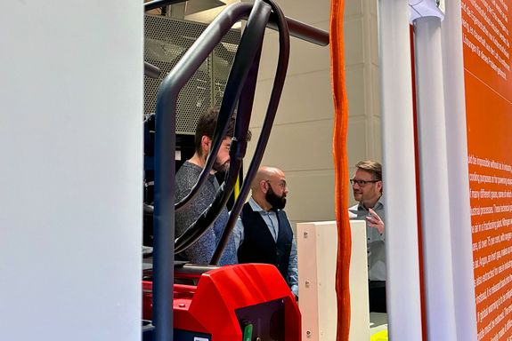 Drei Männer unterhalten sich, im Vordergrund ein paar Kabel und Infotafeln.