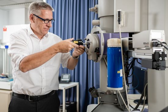 Forscher steht neben einem Elektronenmikroskop