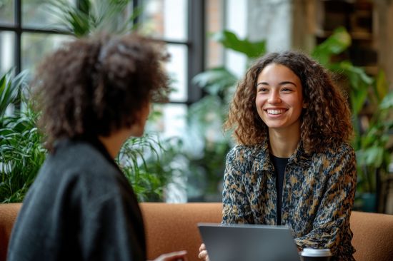Two women of different backgrounds sit opposite each other and talk.