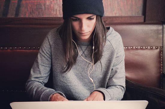 Junge Frau mit schwarzer Haube und Kopfhörern schaut auf Laptopbildschirm. 