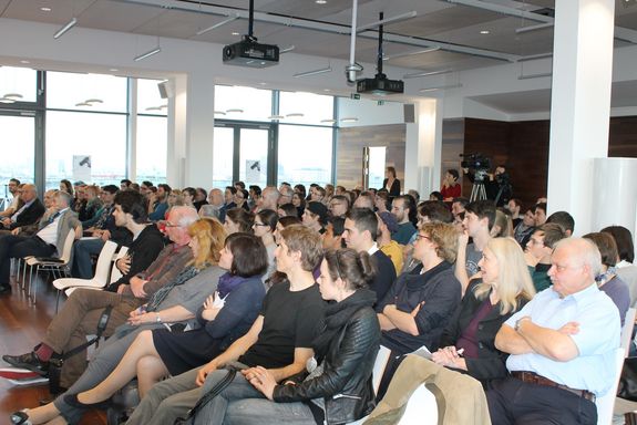 View of the audience, the hall is full. In the background is the cameraman.