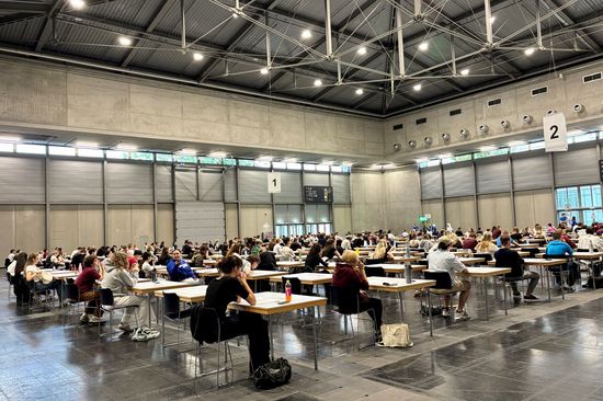 große Halle, Menschen sitzend bei kleinen Pulten
