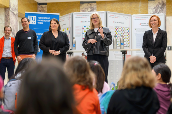 Vizerektorin Steiger, Vizebürgermeisterin Gaál und Bezirksvorsteherin Halbwidl eröffnen den Töchtertag. Sie tragen dunkle Oberteile bzw. Jacken. Von hinten sind die zuhörenden Mädchen erkennbar.