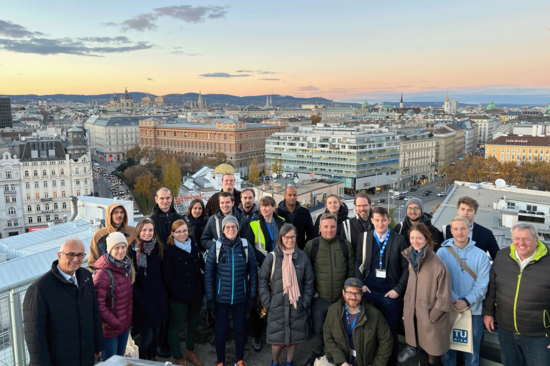 Gruppenfoto am Freihaus der TUW. Die Abgebildeten tragen winterliche Kleidung, der Himmelist hellblau und lachsrosa.