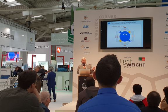 Prof.Dr. Schrödl presents the functionally integrated gear box – a part of the planetary motor – at the forum "integrated lightweight plaza" infront of a group of listeners.