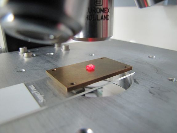 Ein künstlicher Diamant unter dem optischen Mikroskop. Da der Diamant viele Stickstoff Fehlstellen enthält, fluoresziert er in roter Farbe.
