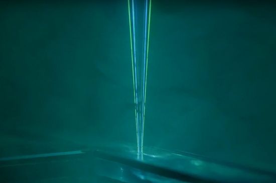 In a dark green environment a light green laser beam  from top side of photo reflecting back upwards   - link to video "Novel Method of Measuring Physical and Chemical Composition in Process Streams"