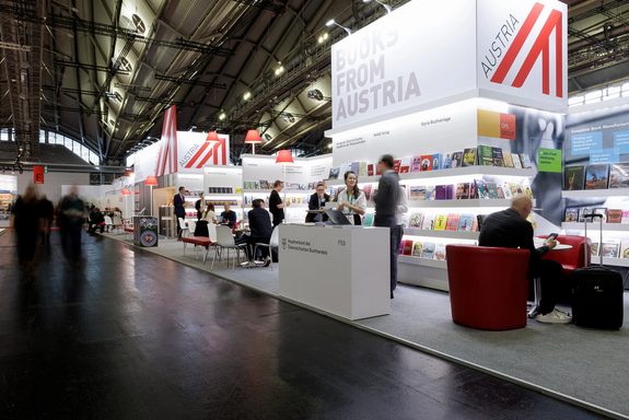 Österreichischer Gemeinschaftstand auf der Frankfurter Buchmesse 2025: Man sieht einen großes Würfel mit "Books from Austria" aufgehängt. Darunter sind viele Regale mit Bücher, Standpulte und Sessel für Gespräche. 