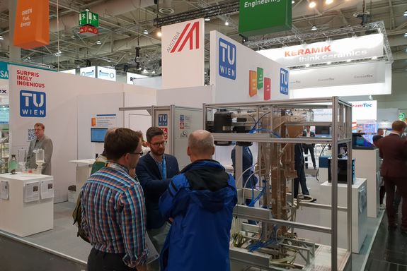 Josef Fuchs (TU Wien) uses the model to explain the dual-bed-fluid gasification to two visitors.