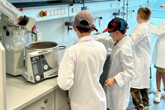 Kindergruppe in Labormänteln mit Schirmkappen im Labor.