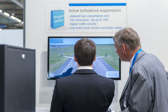 two men infornt of a monitor, one is controling a flight simulator