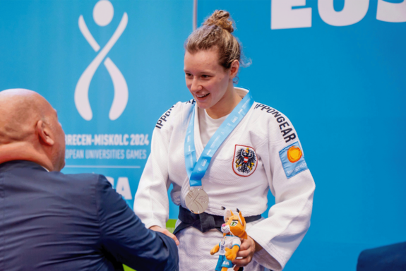 Laura Kallinger im Judoanzug, Silbermedaille mit blauer Schleife um den Hals, wird gratuliert.