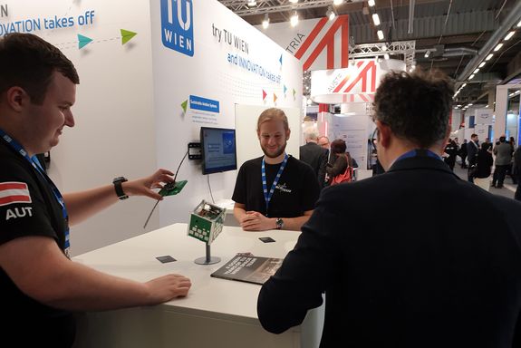 Messestand des TU Wien Space Teams. Drei Personen stehen um den Tisch herum.