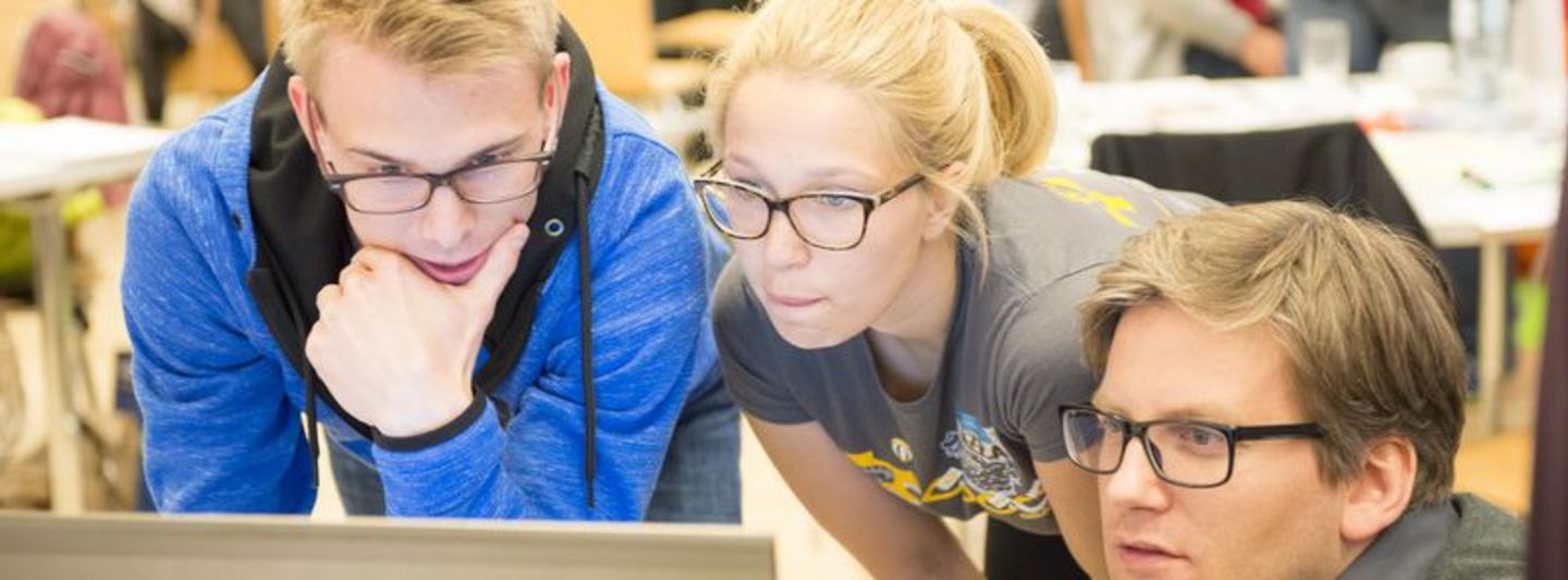 3 Studierende vor einem Laptop