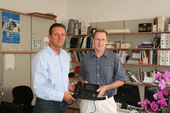 Christian Zander (links), Kapsch BusinessCom, überreicht Prof. Frank Kubel (rechts), E164, sein neues Telefon.