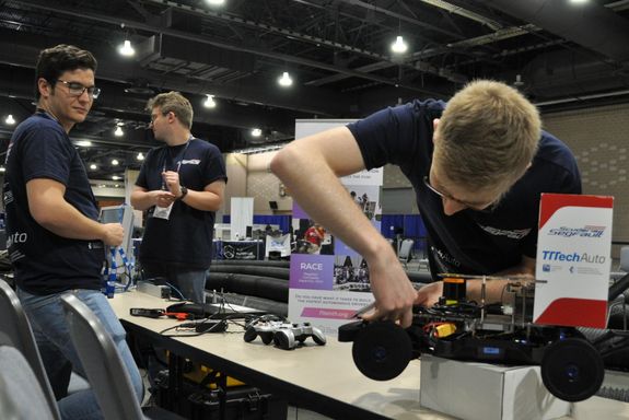 Drei Personen an einem Tisch, die ein Modell-Rennauto reparieren