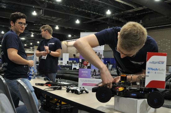 Drei Personen an einem Tisch, die ein Modell-Rennauto reparieren