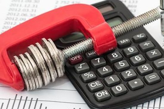 Münzen in einer Schraubzwinge liegen auf einem Taschenrechner