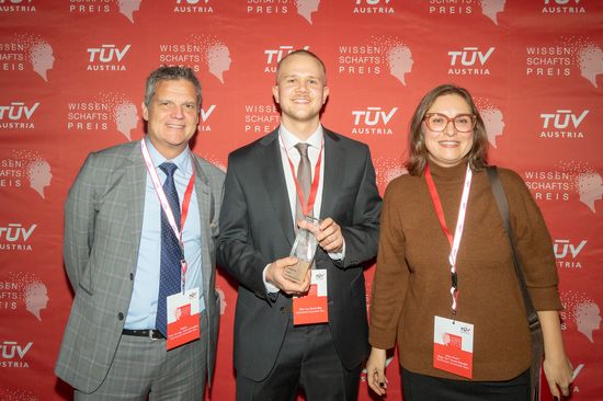 Gruppenbild vor einem TÜV Rollup. Preisträger hält Preis in der Hand. 