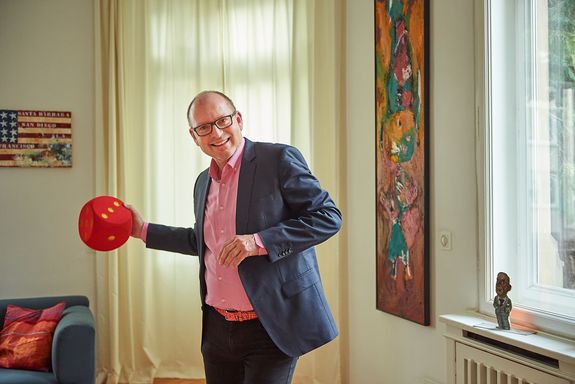 Porträt Christian Hesse stehend mit rotem großem Stoffwürfel in der Hand
