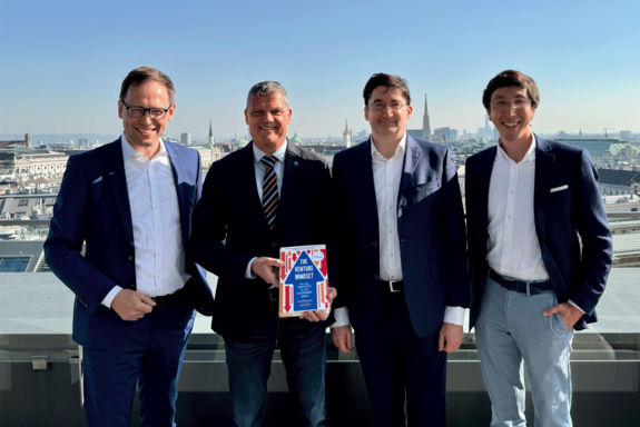 Group photo with four people on a roof terrace. Blue sky and the rooftops of Vienna in the background.