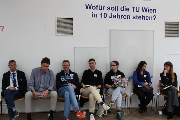 Rektor Schneider und Leitungen der Arbeitsgruppen sitzen nebeneinander an einer Wand