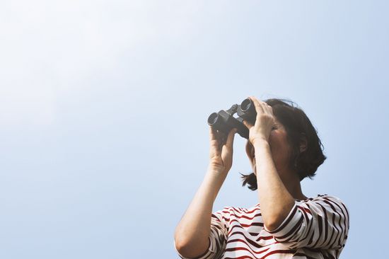 A woman with binoculars in front of a blue sky