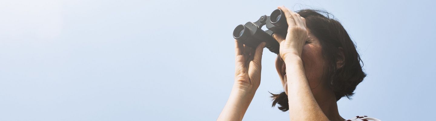 A woman with binoculars in front of a blue sky