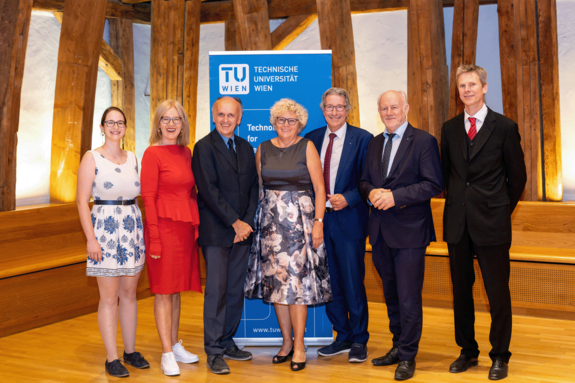 Gruppenfoto mit sieben Personen in feierlicher Kleidung. Im Hintergrund TU-Aufsteller. Ort: TUW-Kuppelsaal mit Holzkonstruktion.