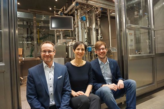 Drei Personen im Labor, dahinter eine Anlage mit Röhren und einem Bildschirm