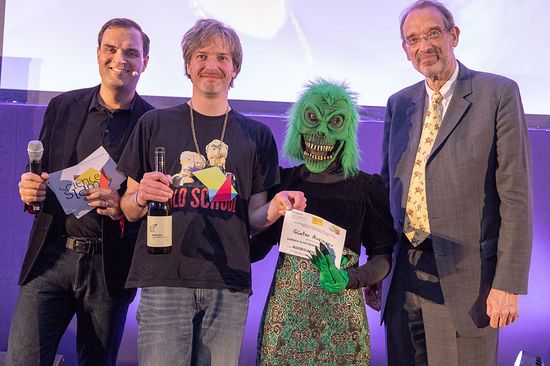 Slam-Staatsmeister 2018 Mathematiker Günter Auzinger (JKU Linz) im Bild mit seinem "Außerirdischen" sowie Wissenschaftsminister Heinz Faßmann und dem Moderator.