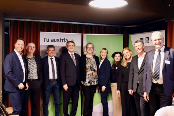 Gruppenfoto mit etwa 15 Personen in Businesskleidung. Dunkler Hintergrund.