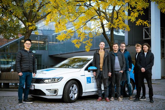Sechs Männer stehen neben einem weißen Auto.