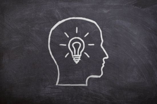 Gezeichneter Kopf mit Glühbirne auf Tafel