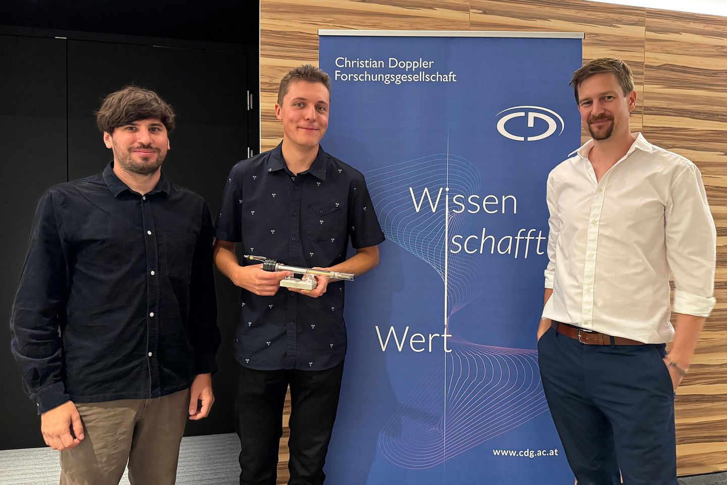 Drei Männer stehen neben einem blauen Roll-up der Christian Doppler Gesellschaft