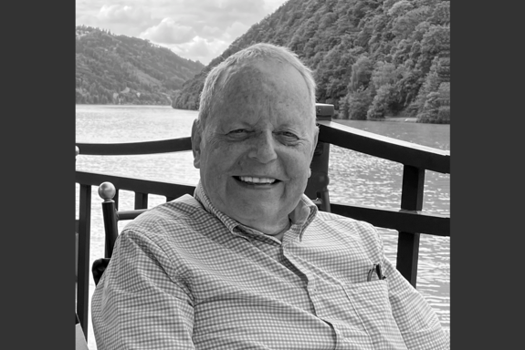 Brustbild, schwarz-weiß, von Prof. Brauner, mit kariertem, hellem Hemd, Flusslandschaft mit Bergen im Hintergrund.