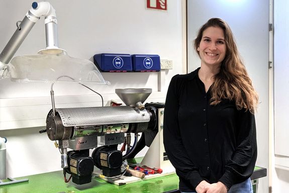 Jessica Schlossnikl in ihrem Labor, sie lächelt, trägt eine schwarze Bluse. Sie steht neben dem Extruder.