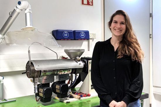 Jessica Schlossnikl in ihrem Labor, sie lächelt, trägt eine schwarze Bluse. Sie steht neben dem Extruder.