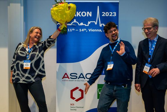 Drei Personen freuen sich über einen Preis und strecken einen Blumenstrauß in die Luft